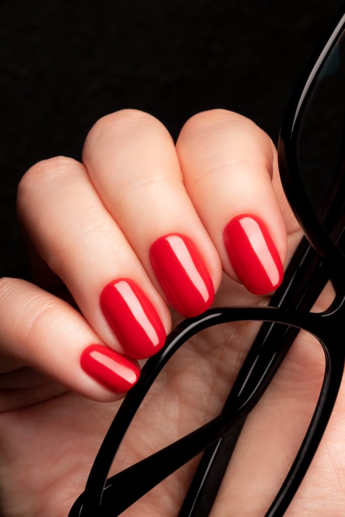 Female hand with beautiful manicure - red nails with glasses on black background closeup