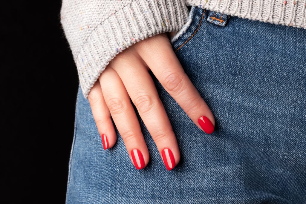 Female hand with beautiful manicure - red nails on jeans denim textile, closeup fingers