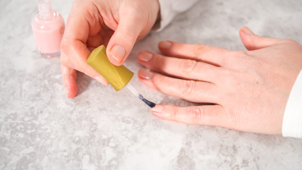 Woman finishing her manicure at home with simple manicure tools. Painting nails with fresh nail polish. Keep Nail Polish from Peeling. Quick Fixes for Peeling Nail Polish.