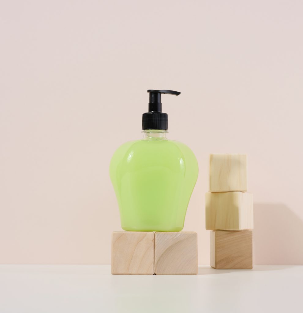 Transparent plastic bottle with green liquid on a wooden podium. Container for cosmetics. Liquid and bar soaps,