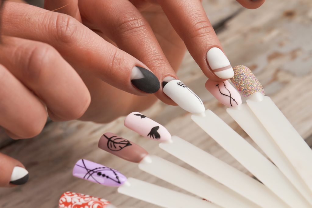 Woman in nail salon choosing nail design. Close up of female hands selects nail color and design close up. Top 2025 Nail Designs.