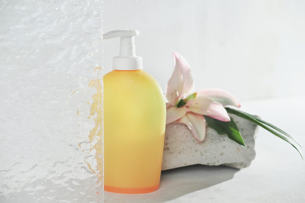yellow unbranded bottle of cosmetic product in bathroom with water drops. floral fragranced shower gel or shampoo in a bottle with pump. self care routine and hygiene.