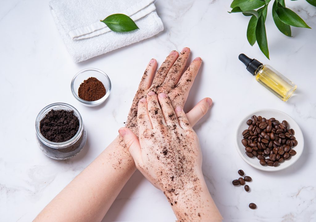One hand puts a peeling on another, isolated. Home spa care for the skin of hands and nails. A young woman does a hand massage with a homemade coffee scrub with olive oil on marble background. Top view. Body Care Hacks.