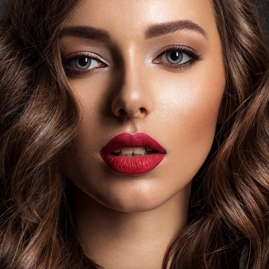 Beautiful face of young woman with red lipstick. Portrait of a stunning sexy girl looks at camera. Attractive model with stylish makeup.  Closeup portrait of a caucasian female.