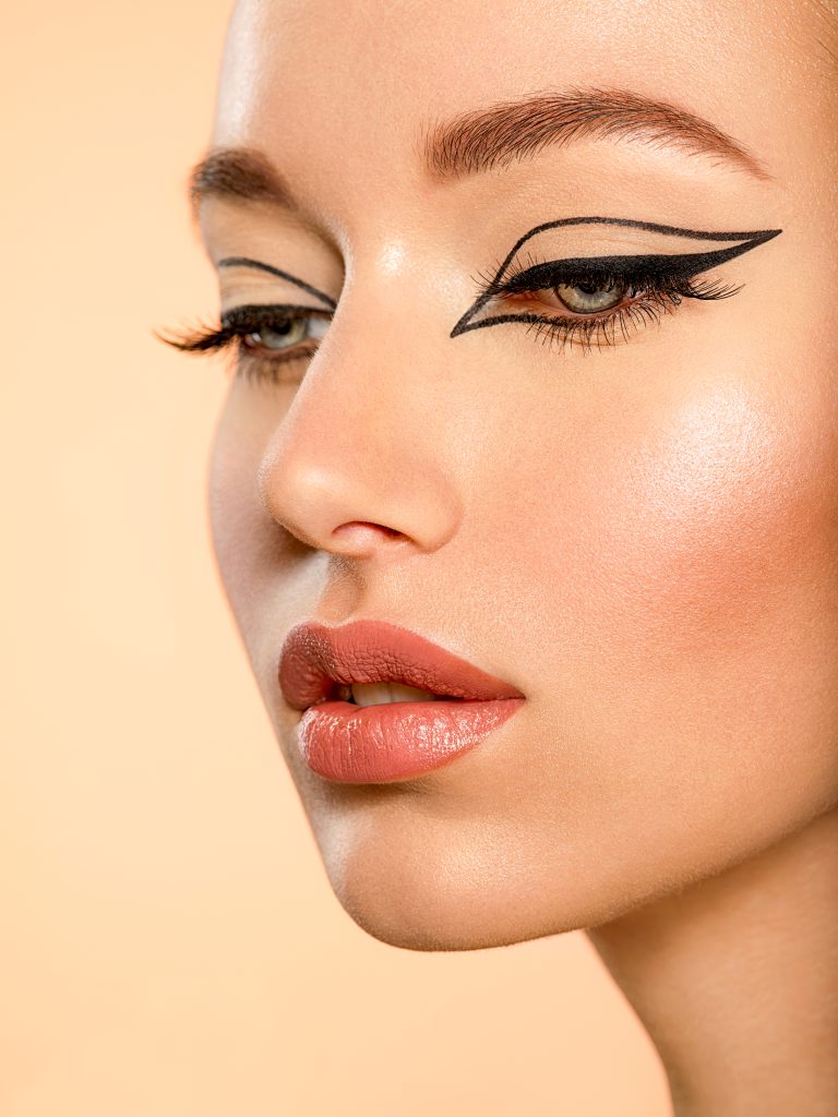 Beautiful girl with makeup in the form of arrows. Face of a young girl close-up with fashionable makeup over beige background. Stylish makeup. winged eyeliner.