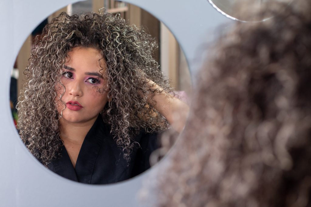 Beautiful latina woman with curly hair looking at herself and posing in the mirror.