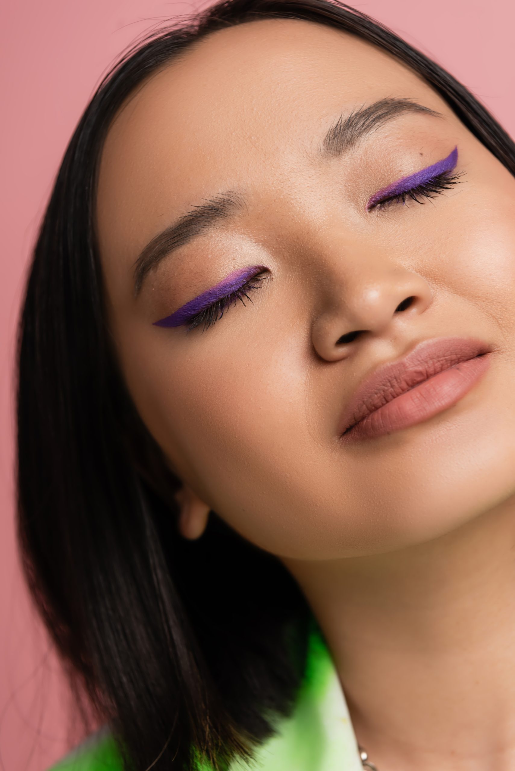 close up view of young asian woman with perfect makeup with blue eyeliner isolated on pink. winged eyeliner.