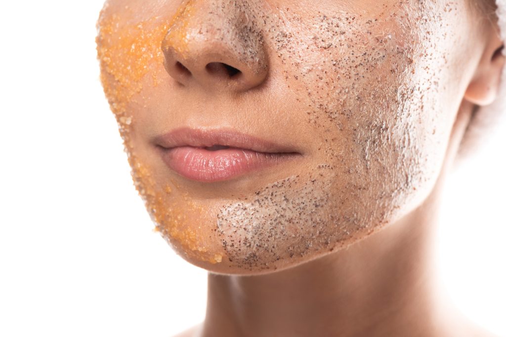 cropped view of young woman with scrub on face isolated on white