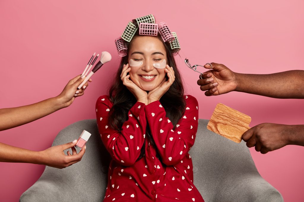 10 Genius Beauty Hacks That Will Change Your Routine. Delighted cheerful woman with natural beauty, smiles gently at camera, enjoys beauty treatments in spa salon, surrounded by beautician hands with cosmetic products, sits in comfortable armchair.