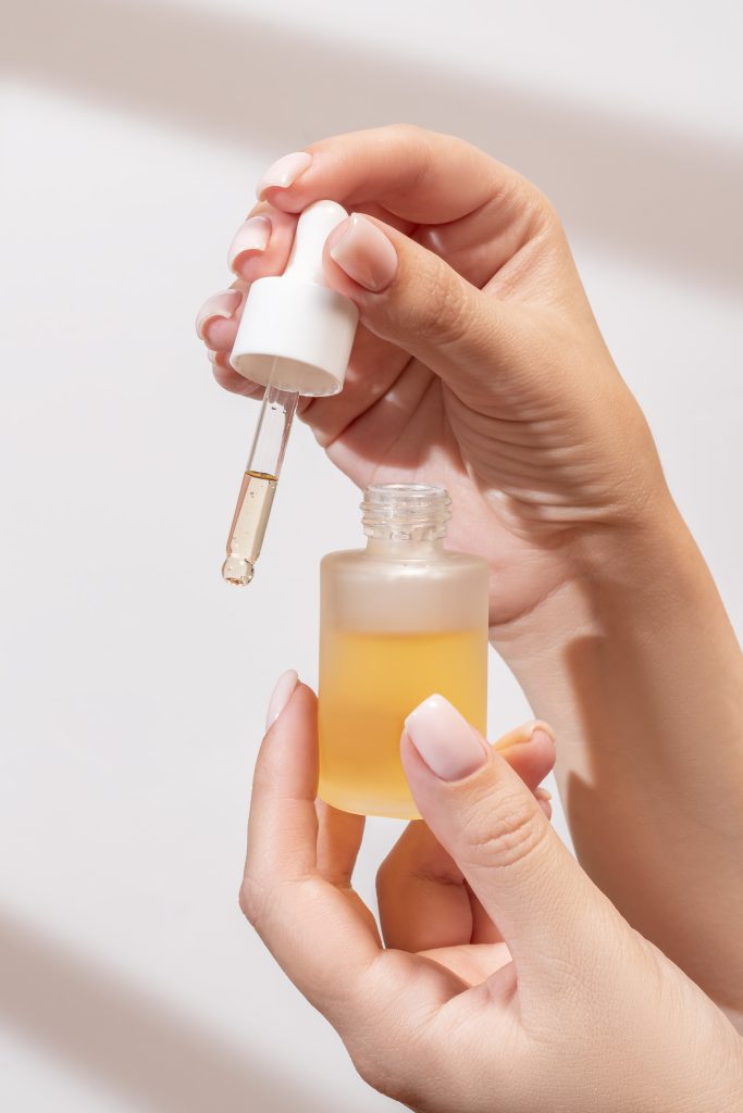 Cuticle oils. female hand with Dropper of essential oil, aromatherapy essence, beauty serum or medicinal liquid on light background with shadows. Unbranded bottles for your design. nail care. hand care.