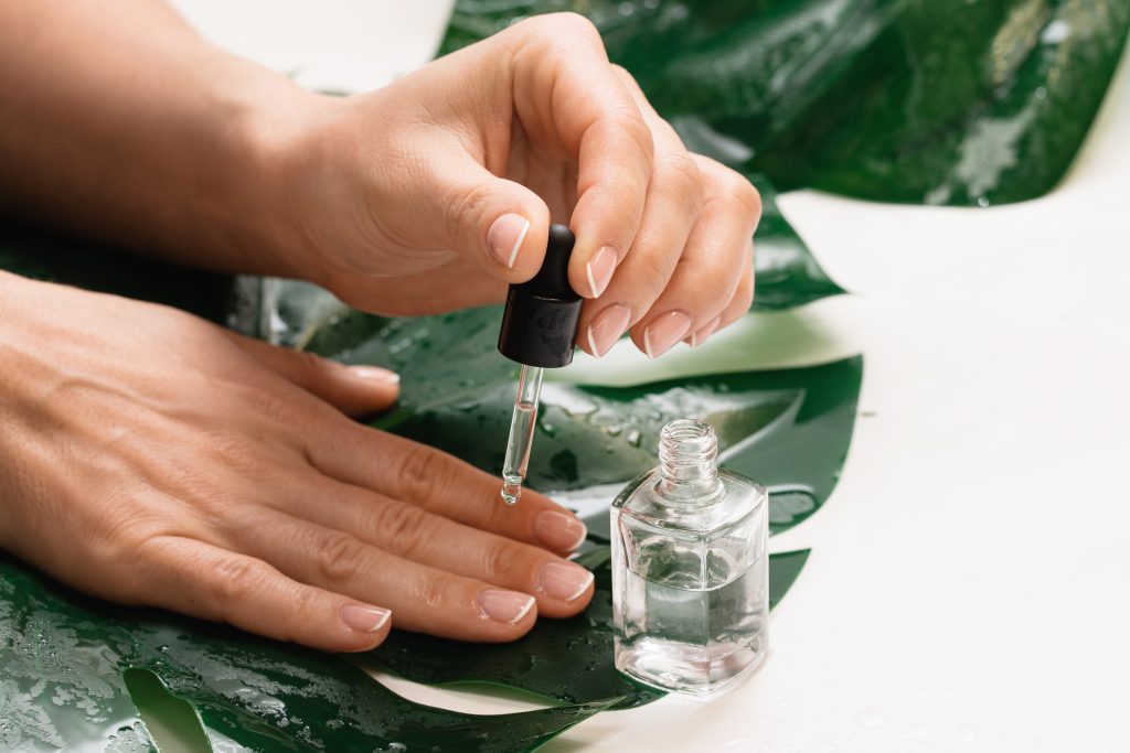 Closeup of female hands and bottle of nourishing cuticle oil with dropper. 