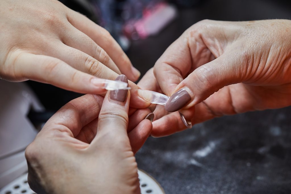 Close-up of a nail technician applying a nail extension to a client's finger in a professional salon. nail tips. nail care. Nail adhesive.