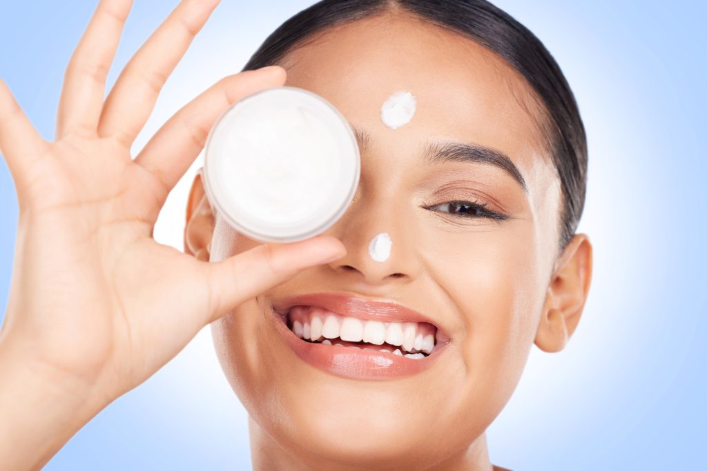 Portrait, happy woman and cream container for face, aesthetic skincare and shine on blue background. Common skincare mistakes