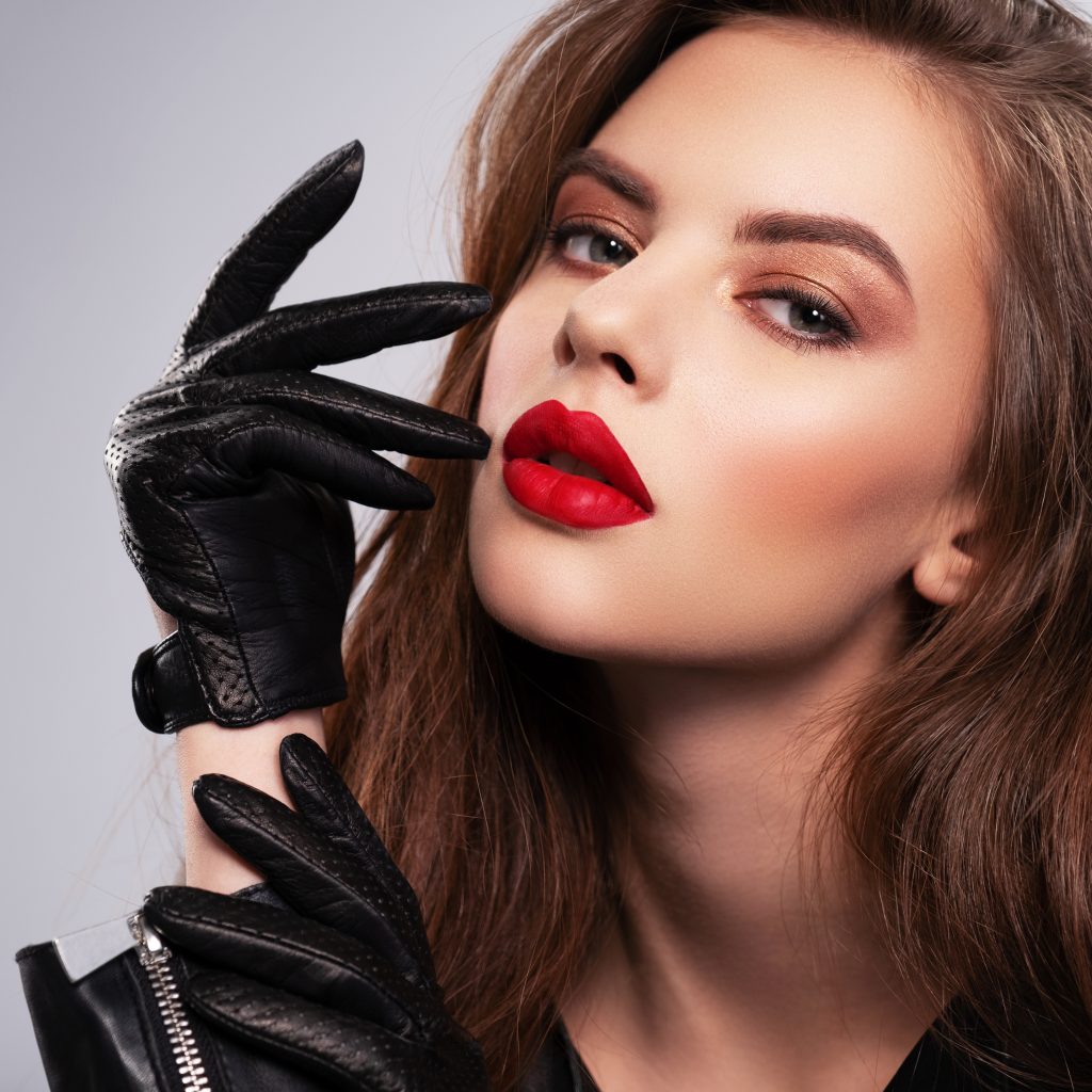Portrait of beautiful young woman with bright makeup. Beautiful brunette with bright red lipstick on her lips. Pretty girl with long brown hair. Brunette dressed in a black leather jacket.