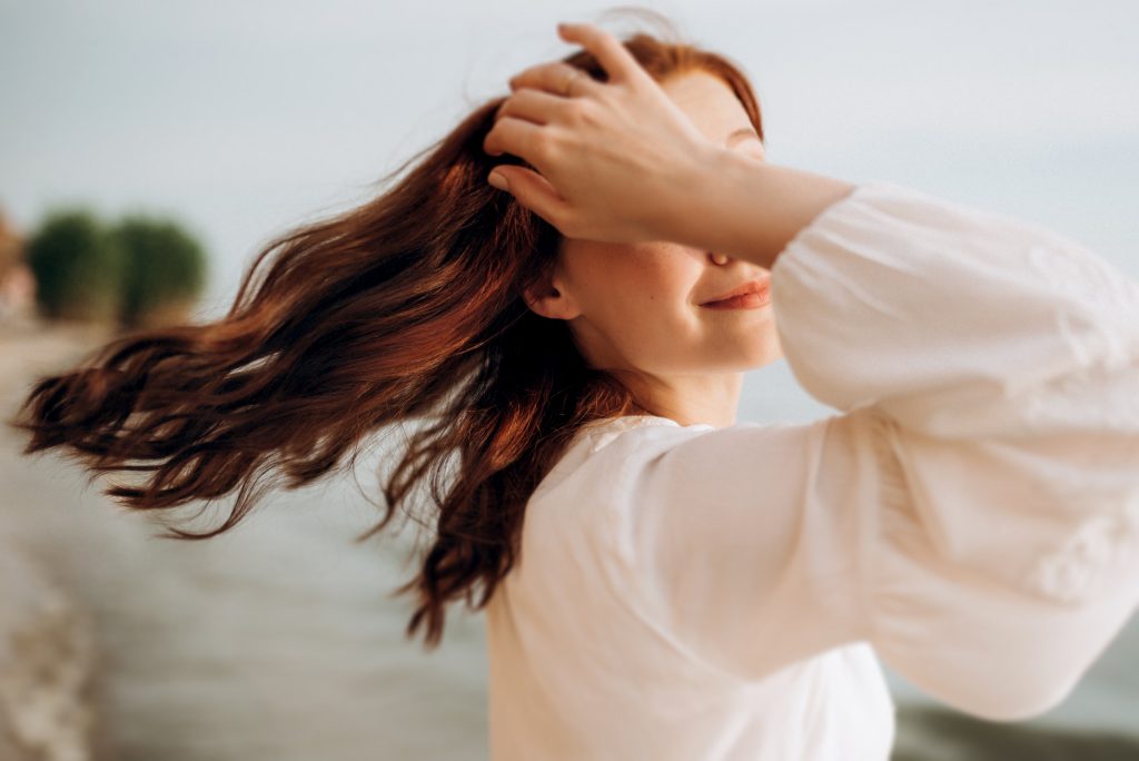 pregnant girl with brown hair on the seashore in white clothes. Nourishing Hair from the Inside Out.