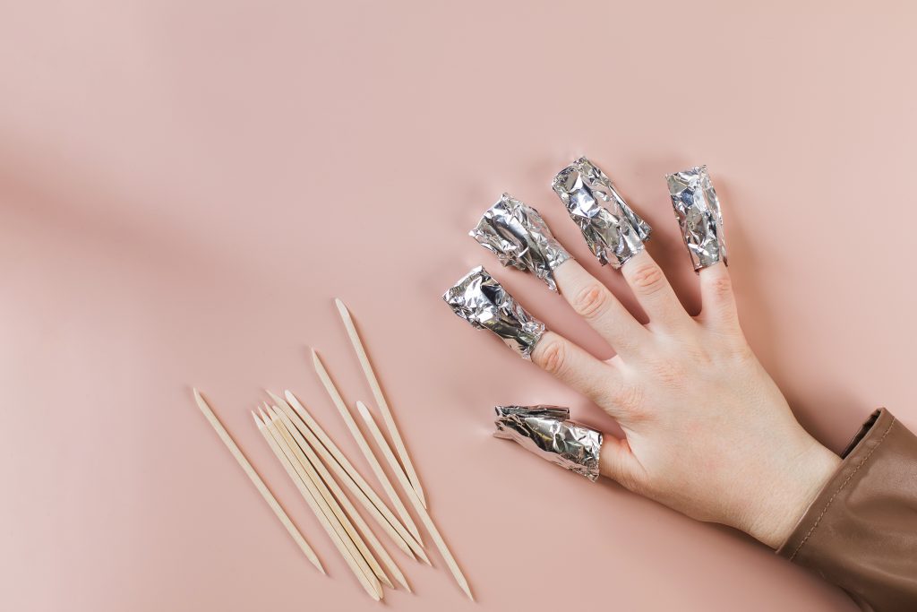 The process of removing gel polish from nails. Nails are wrapped in falga on a pink background. Copy space. High quality photo. remove nail glue. remove nail adhesive.