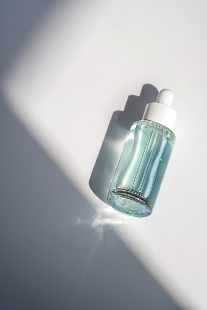 A blue transparent bottle with serum in the rays of the sun. Laconic bottle shape.