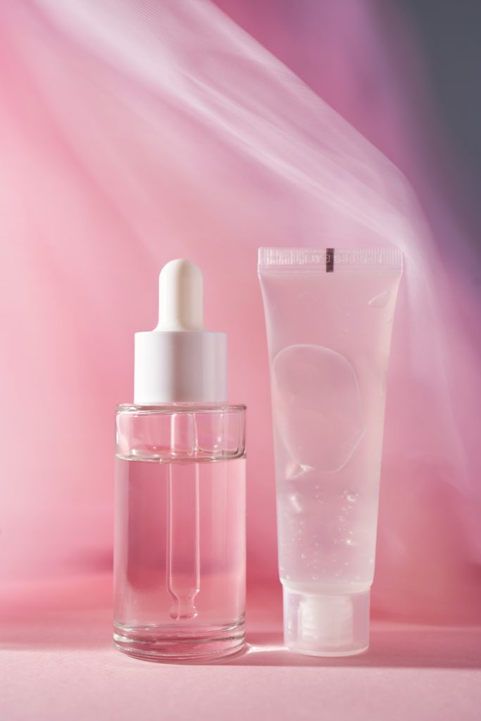 A transparent bottle of cosmetic gel and a bottle of serum on a pink background. Gentle photo of cosmetics.