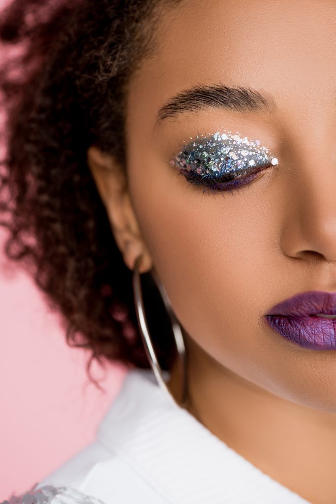 beautiful african american girl with silver glitter eyeshadows and purple lips, isolated on pink