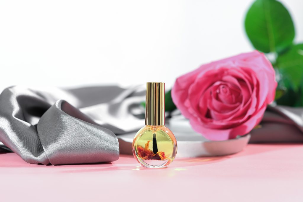 cuticle massage oil with rose petals infusion. pink rose flower next to a bottle of nail care oil, hans and nails beauty care, skin moisturizing and nourishing, spa manicure concept