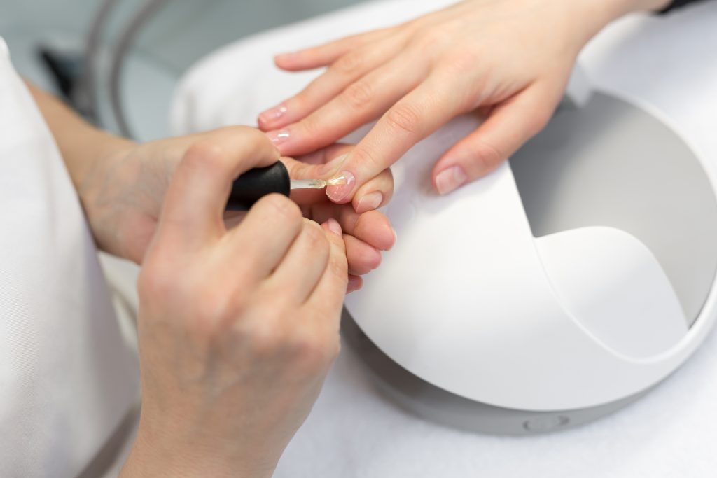 Girl paint nails in the salon of manicure, close-up. Master applies varnish on nails in manicure salon. Woman getting nail manicure in salon. Care for hands