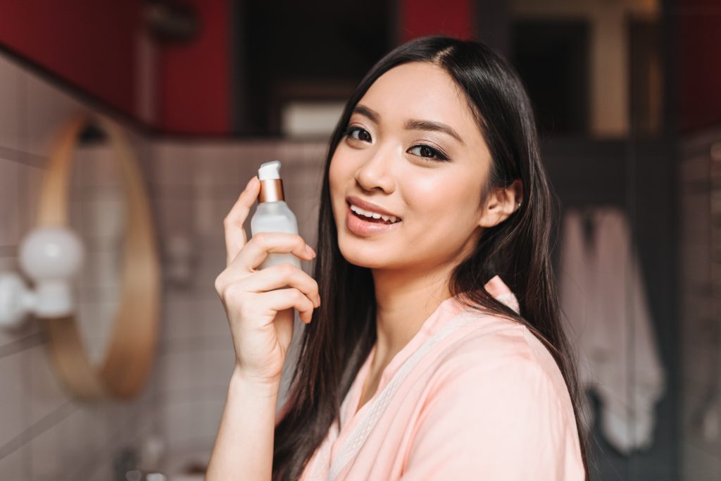 Lady holds jar of serum for face. Woman cute smiling against bathroom. face toner. facial care, toner