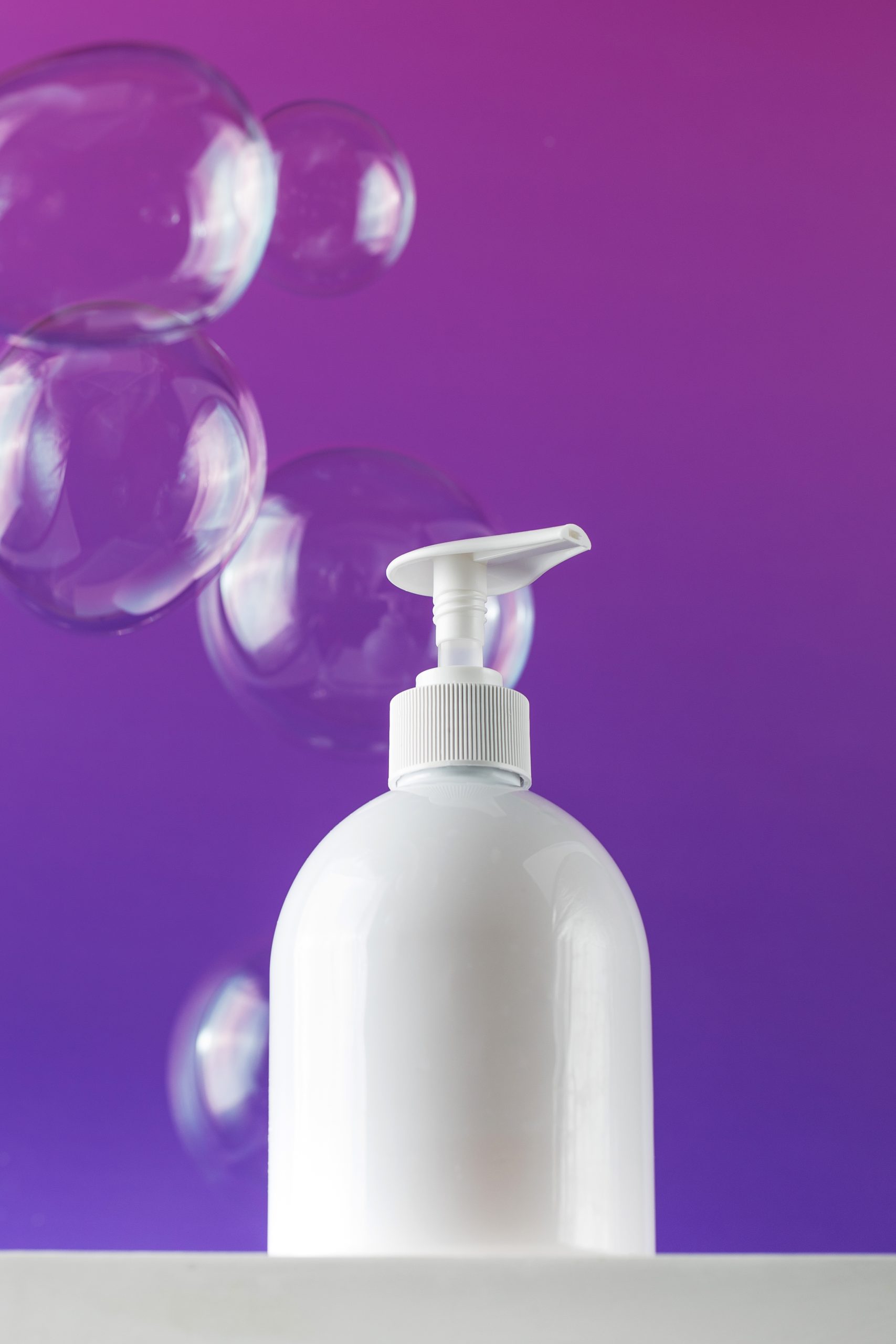 Body Shower Gel. Mockup of a white dispenser with a cosmetic product such as soap, shower gel on a pedestal on a purple background and flying soap bubbles around.