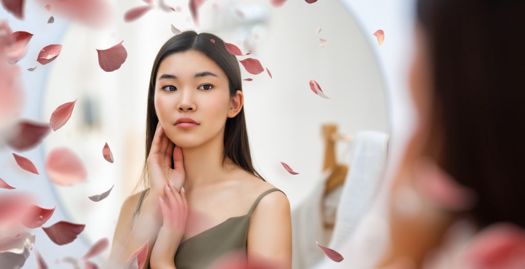 Portrait of attractive young woman looking at mirror. Beautiful girl enjoying her reflection, self-care concept.