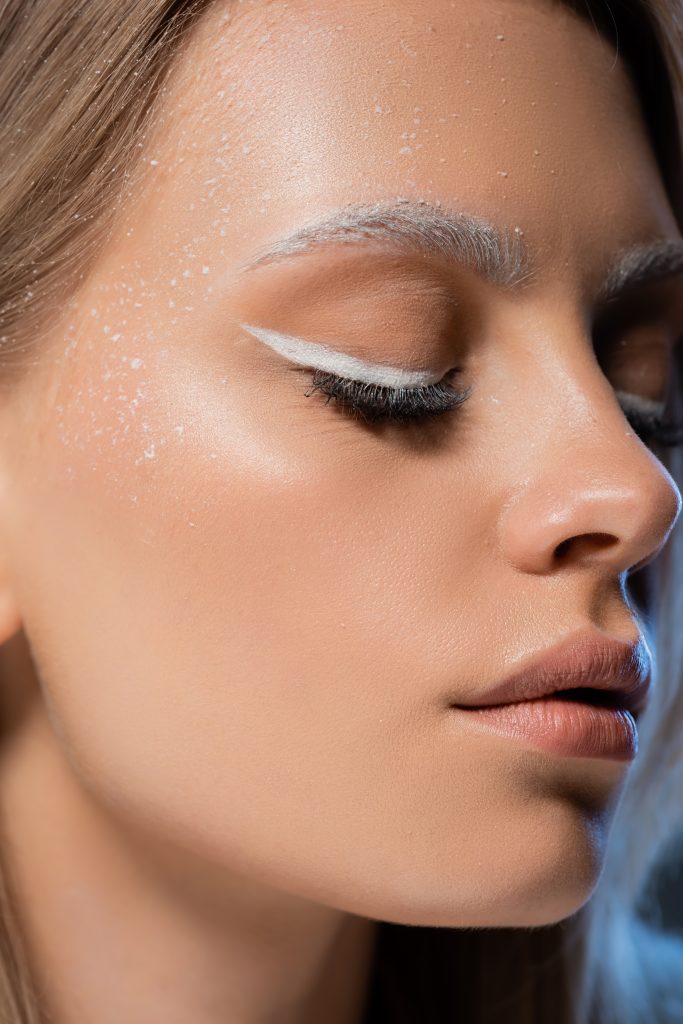 close up view of blonde young woman with winter makeup and closed eyes. white eyeliner