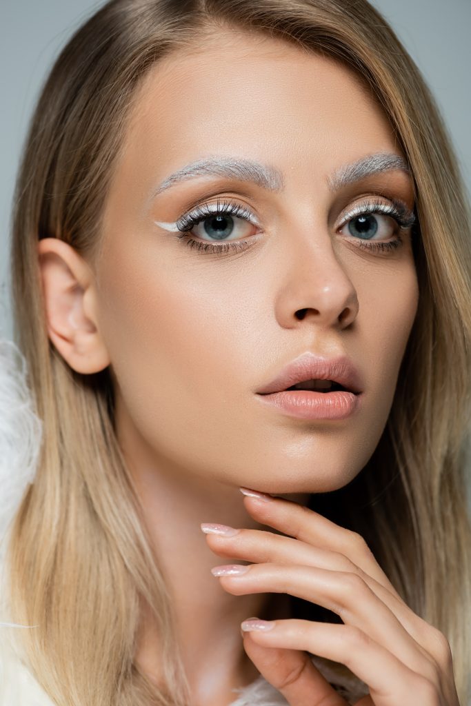 close up view of young model with winter makeup and frozen white eyebrows isolated on grey