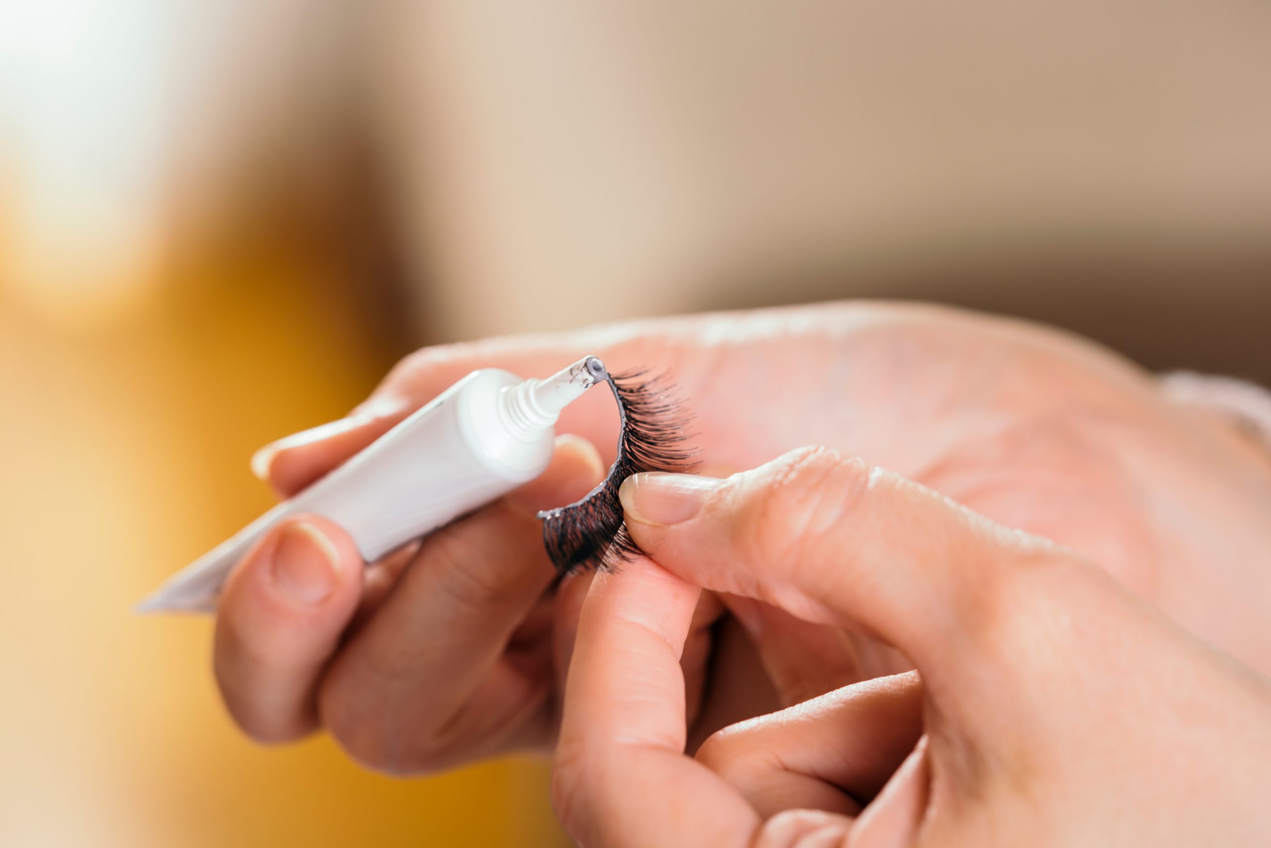 Detail of make up artist's hands adding glue on artificial eyelashes while doing a client's make up. lash glue. lash adhesive. Best Lash Glue. Lash Glue Top Picks.