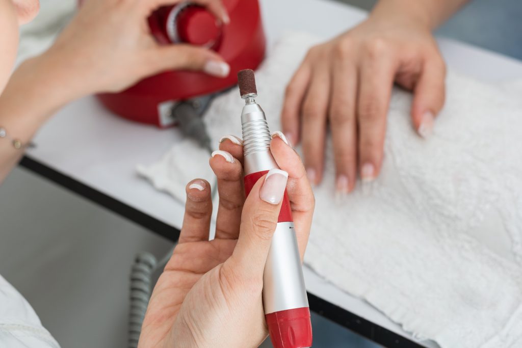 detail of the manicurist's hand holding the electric nail buffer ideal for sanding, polishing acrylic nails, gel nails, artificial nails, natural nails and pet nails. checking for proper operation.