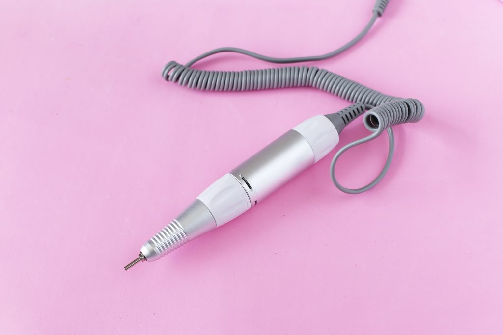 Special handle with a ceramic cutter for a professional female manicure and pedicure on a pink background. Specialized equipment for nail service