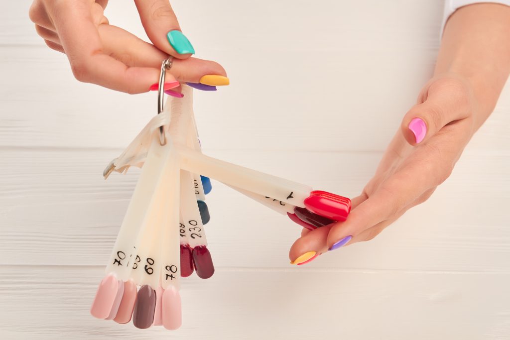 Well-groomed hands holding nail color samples. Nail samples painted with bright varnish in female manicured hands. Nail beauty salon.