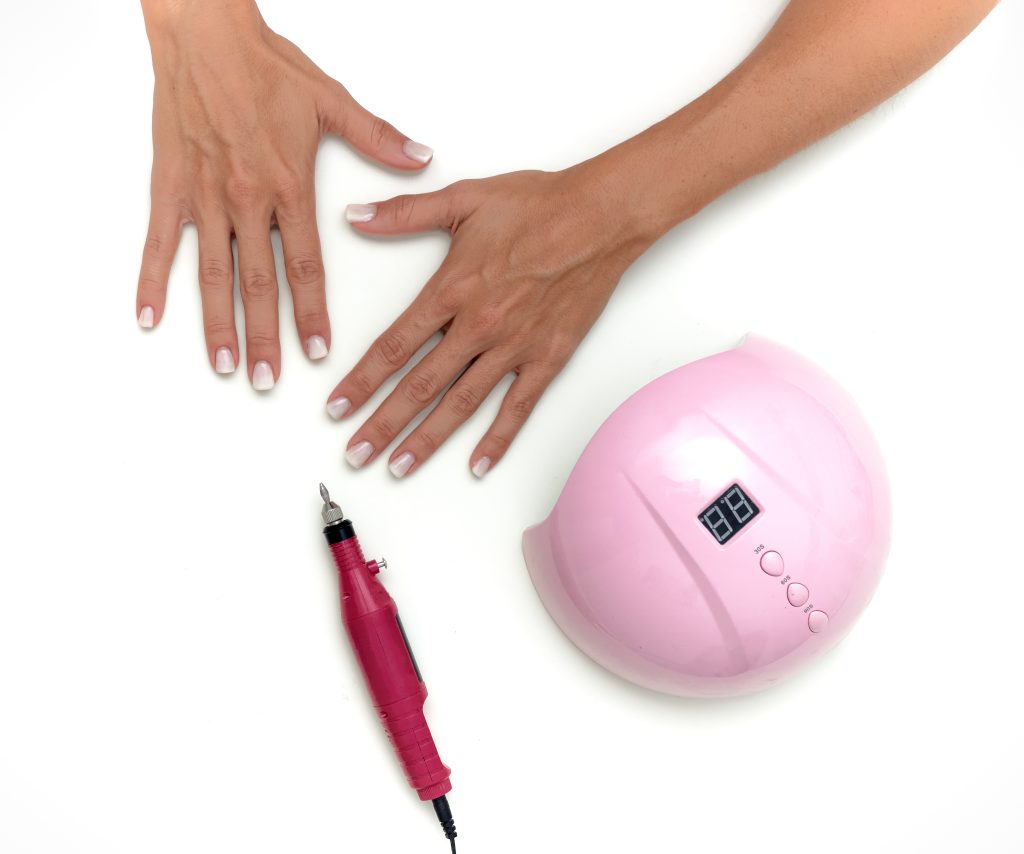 cordless nail drills. Young white female hands with newly done nail manicure on a white background.