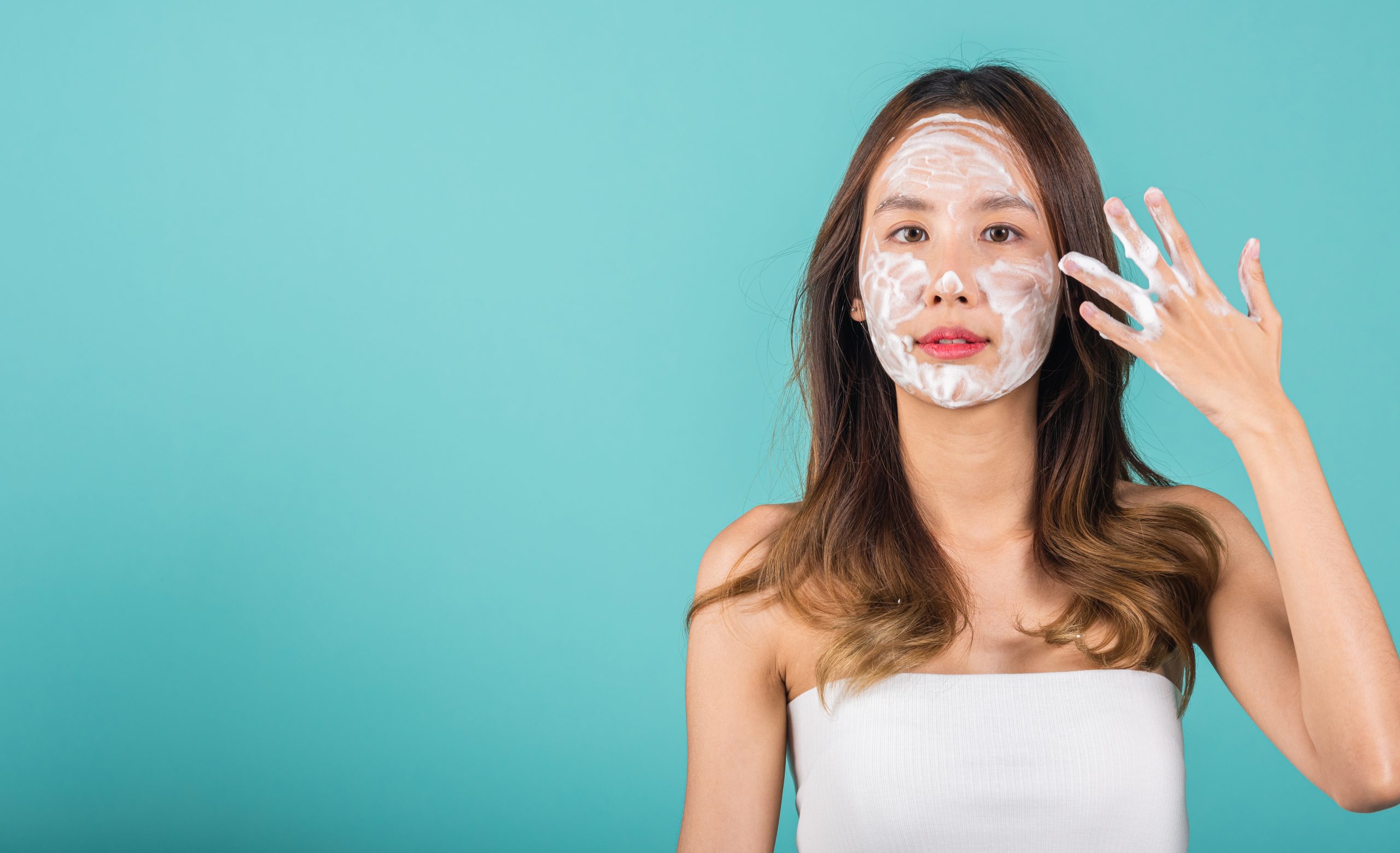 Double Cleansing. Asian woman face wash exfoliation scrub soap with skincare cleansing, Portrait beautiful female smile applies foaming cleanser healthy skin, Studio isolated on blue background, skincare daily routine
