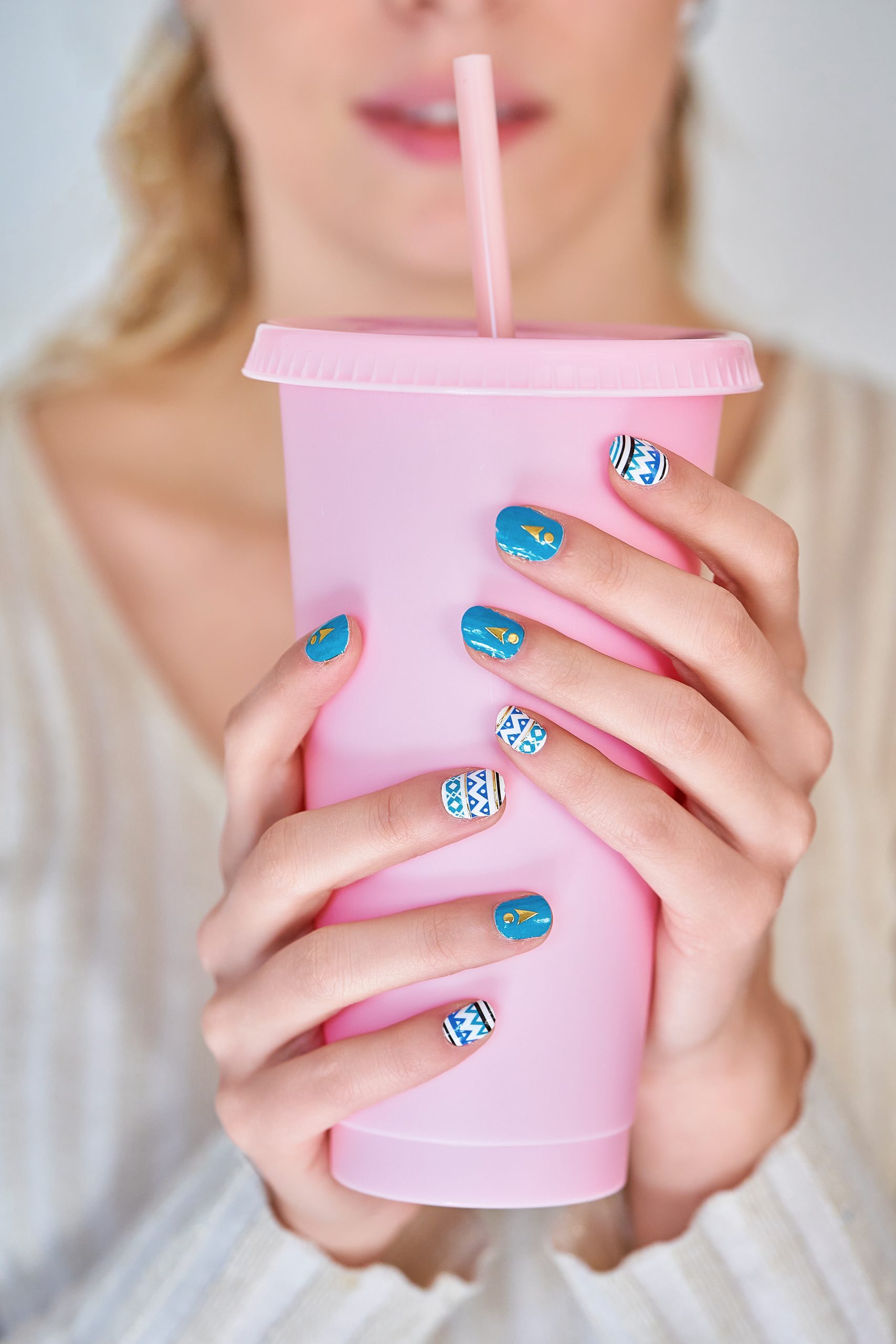Close-up of a woman with colourful manicure nails holding plastic cup. Manicure and beauty concept.. summer 2025 manicure. summer nails. 2025 nails. nail polish shades for 2025.