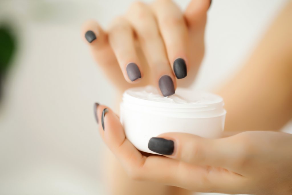 Cream for face or body in white container on female hands.