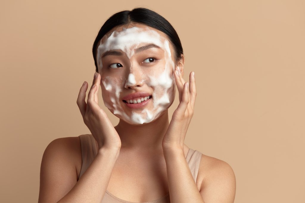 Double Cleansing. Face Skin Care. Cute Asian Woman Cleaning Facial Skin with Foam Soap. Happy Girl Cleansing Face Applying Facial Cleanser Closeup. High Resolution