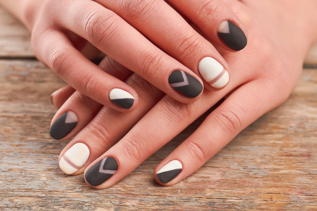 Matte Top Coats. Female hands with stylish manicure. Woman hands with black and white matte manicure on old wooden background close up. Salon beauty and spa.