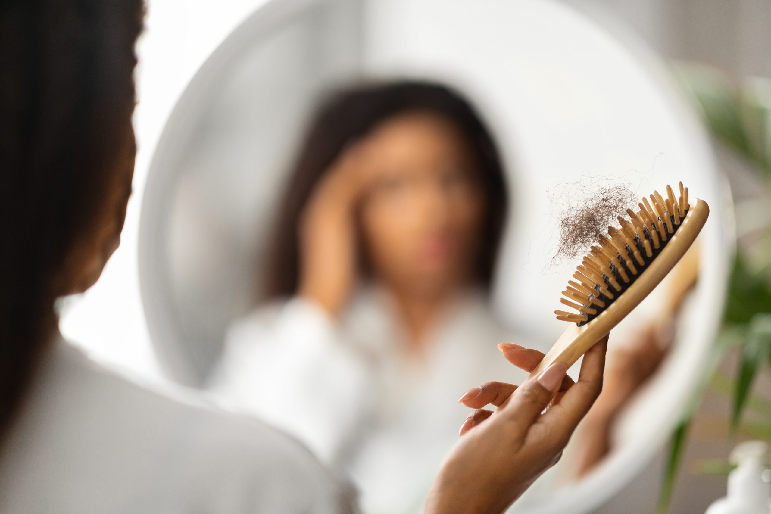 Hair Loss Causes. Hairloss Concept. Upset Black Woman Holding Comb Full Of Fallen Hair After Brushing, Closeup Shot Of African American Female With Brush In Hand Standing Near Mirror, Suffering Alopecia Problem. hair loss causes. hair loss.