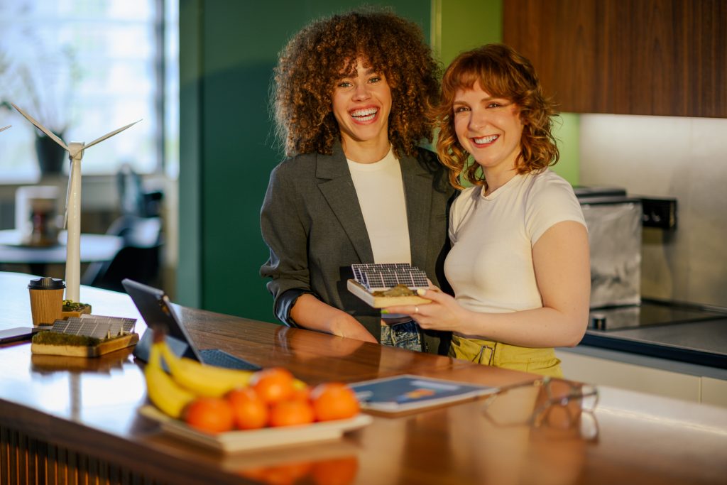 stress affects your skin. Portrait of two happy environmentalists standing at modern office with solar panels model in hands and smiling at the camera. Young female ecology experts working on sustainable and renewable energy.