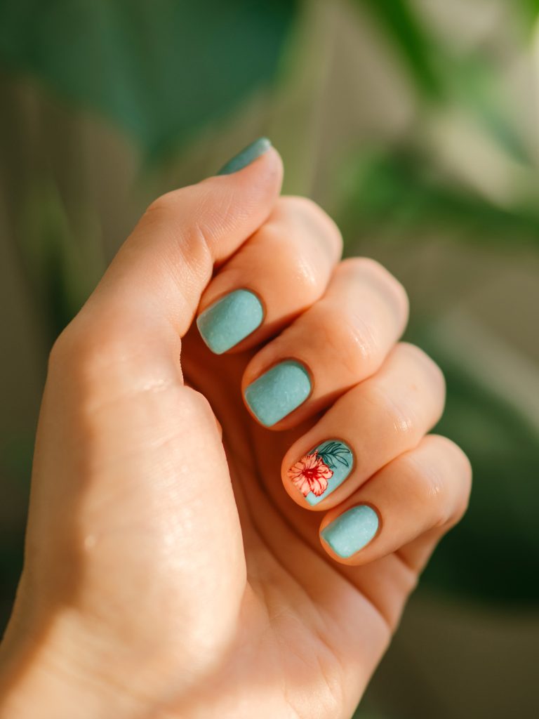 Matte Top Coats. Aesthetic visual of fingernail with short nail with blue teal manicure with reverse stamping summer tropical flower. Nail closeup with stylish pink flower in reverse stamping nail art design manicure.