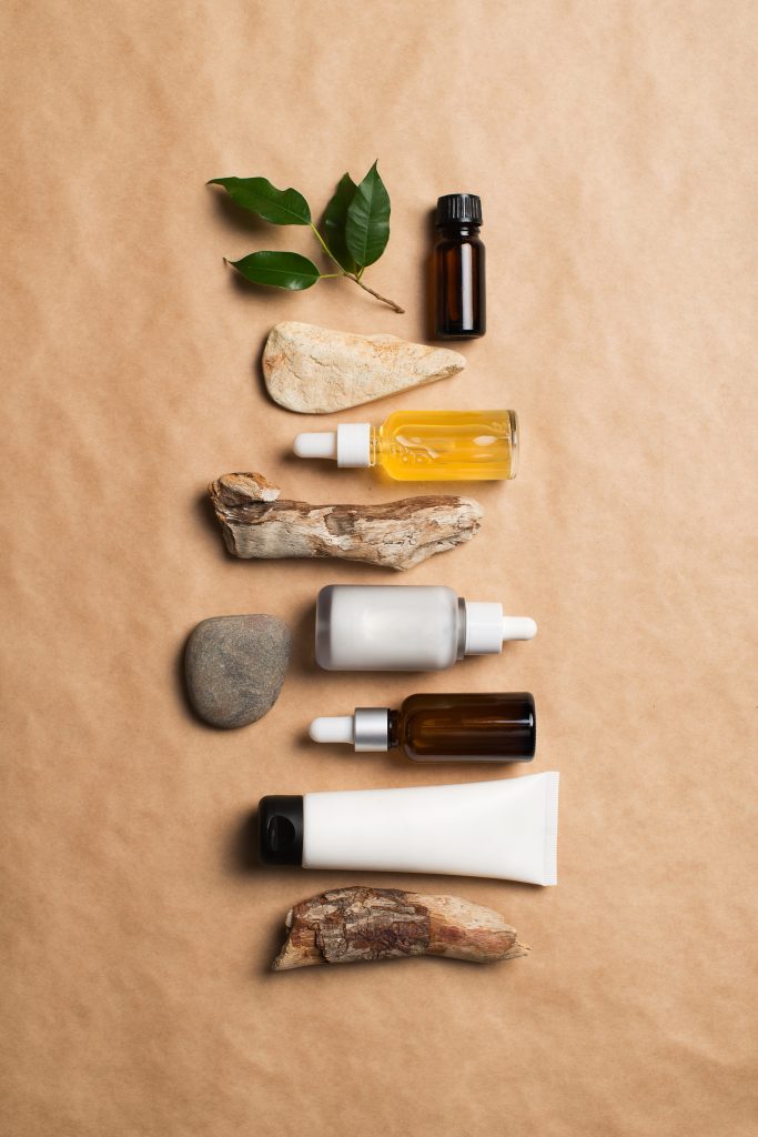 Serum bottles natural organic cosmetic with green leaf on brown, copy space, top view, knolling, vertical
