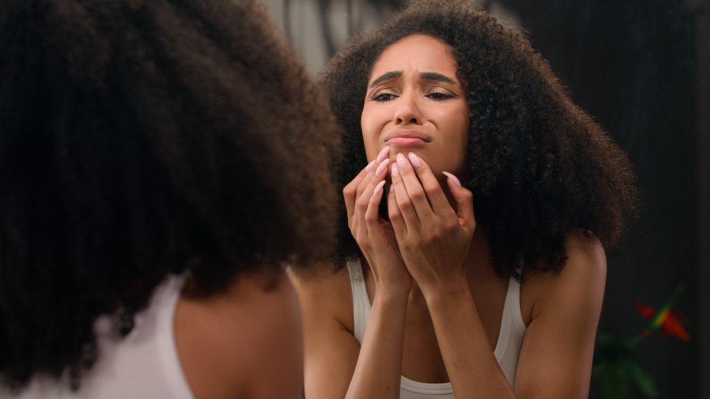 stress affects your skin. Worried young beautiful African American woman sad ethnic girl looking in mirror stressed about facial wrinkles problem acne frustrated upset touching face dry sensitive skin care facial blackheads. High quality 4k footage