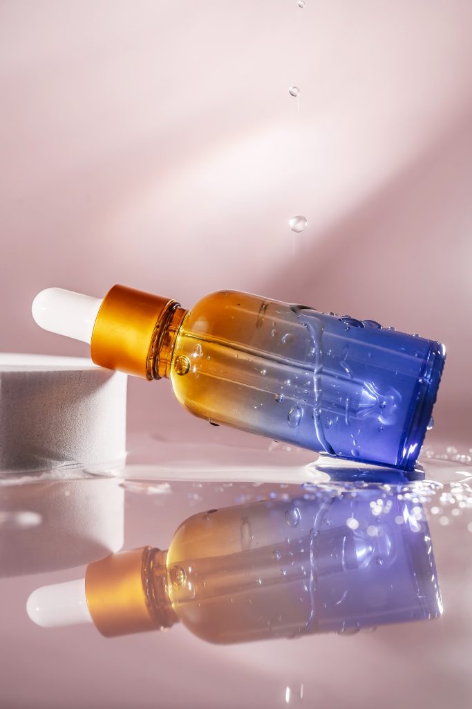 Cosmetic bottle with water splashes on a pink background. Front view. Perfectly emphasizes the moisturizing function of the serum.