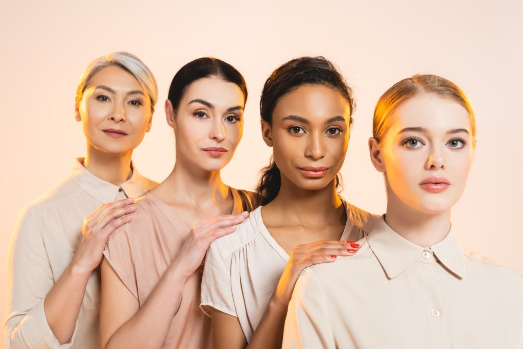 skin types. four beautiful multicultural women looking at camera isolated on beige