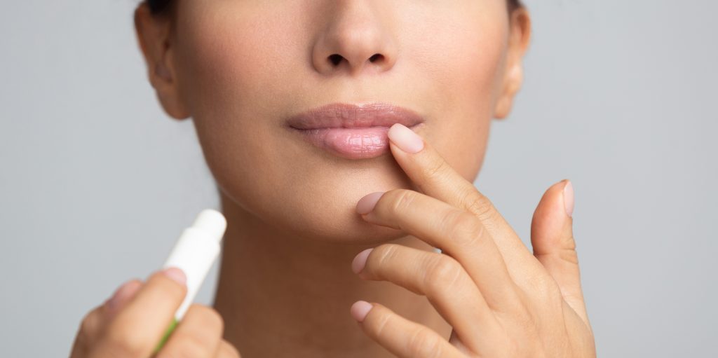 Lips skin care. Afro woman applying balsam over grey studio background, panorama