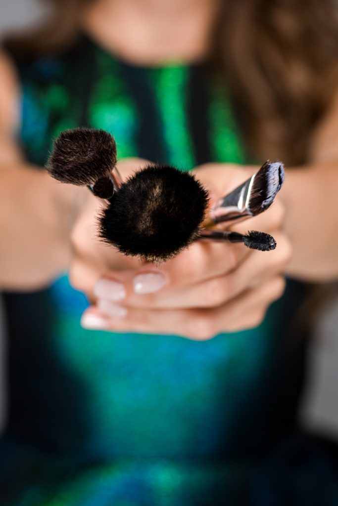 partial view of woman showing makeup brushes in hands