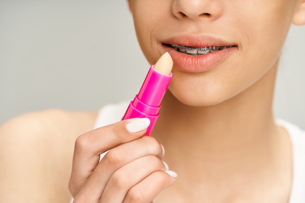 A stylish teenage girl in vibrant attire holds a pink lipstick, exuding confidence and glamour.